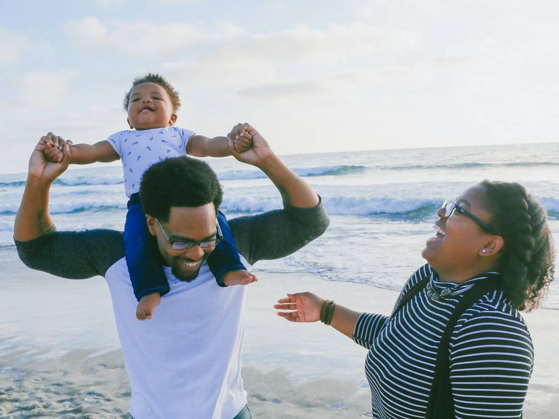 A family on the beach, father carrying a child on his shoulders