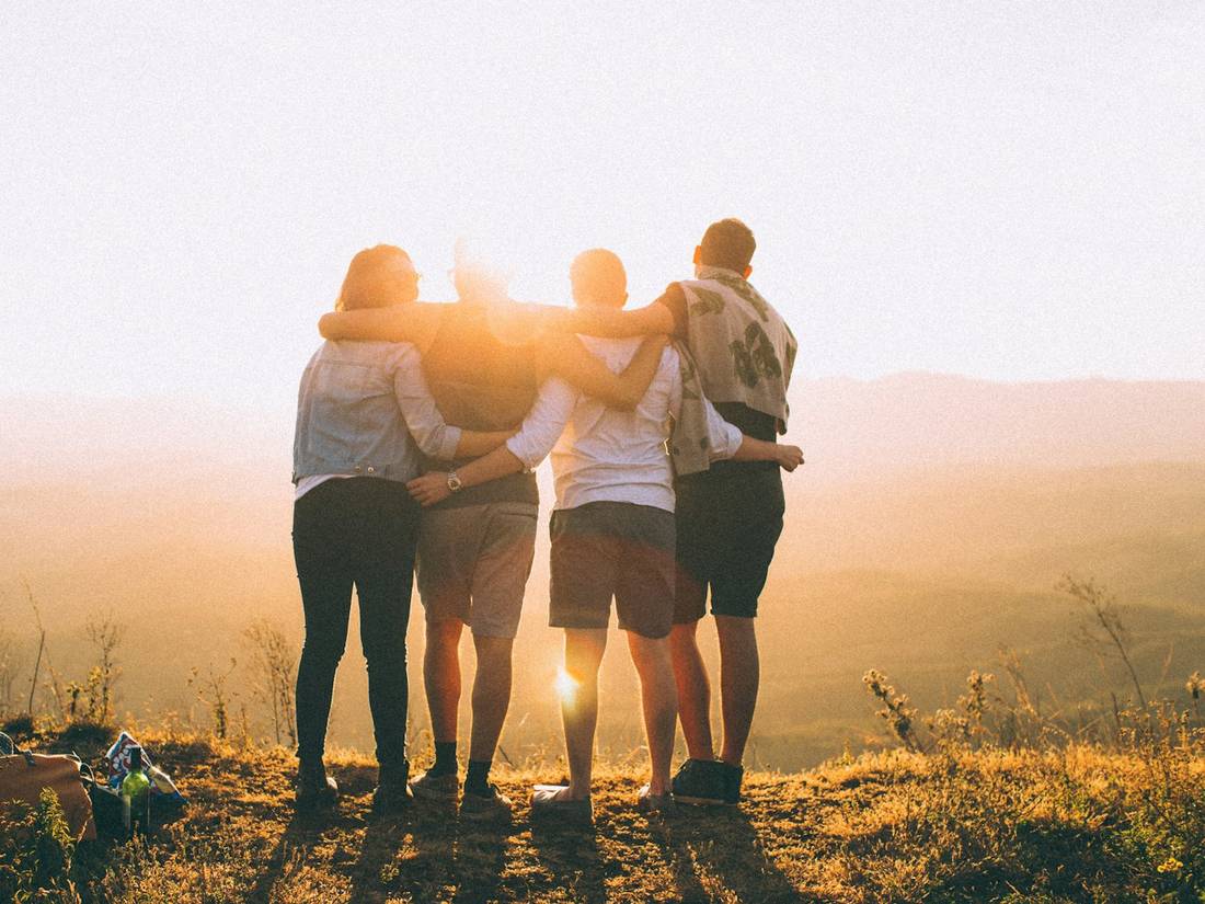 Friends with arms around each other watching the sun
