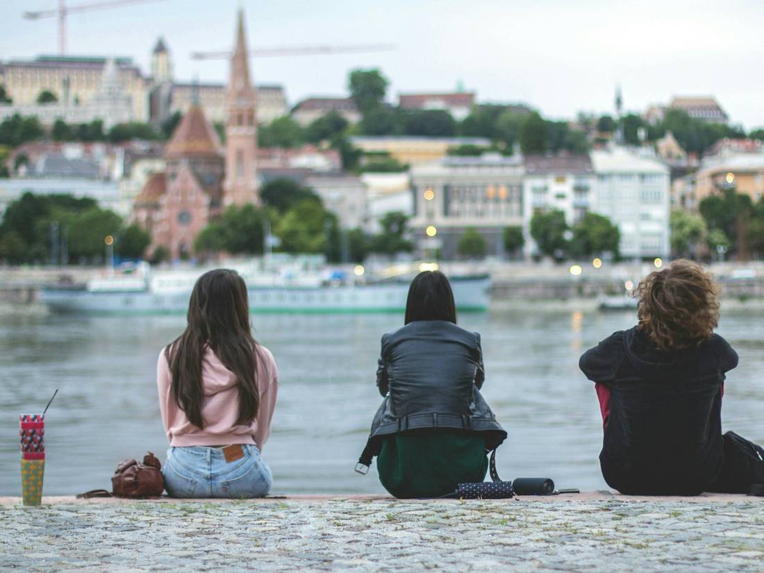 Three friends sitting by a river overlooking a city